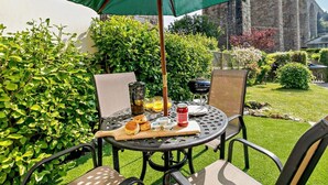 Een ronde metalen tafel met een groene parasol, een barbecue en eten.
