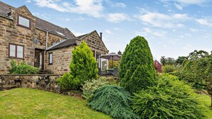 A stone house with a well-maintained lawn, a tall coniferous tree, and a small pond. - 2 Bed in Matlock (oc-92639) (Holloway)