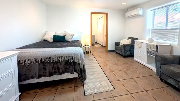 Ein Schlafzimmer mit Bett, Nachttisch, Schminktisch und einem Fenster mit Jalousien.