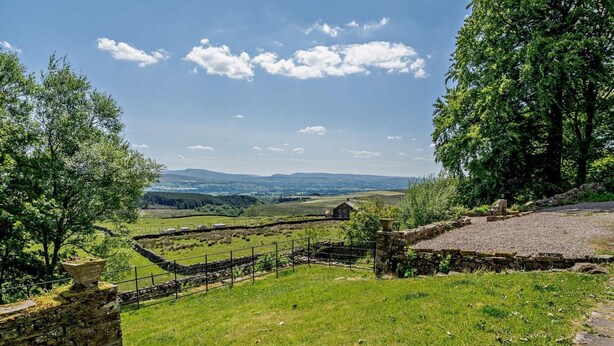 Un paysage rural avec des murs de pierre, une zone délimitée par une clôture et une vue sur des collines lointaines.