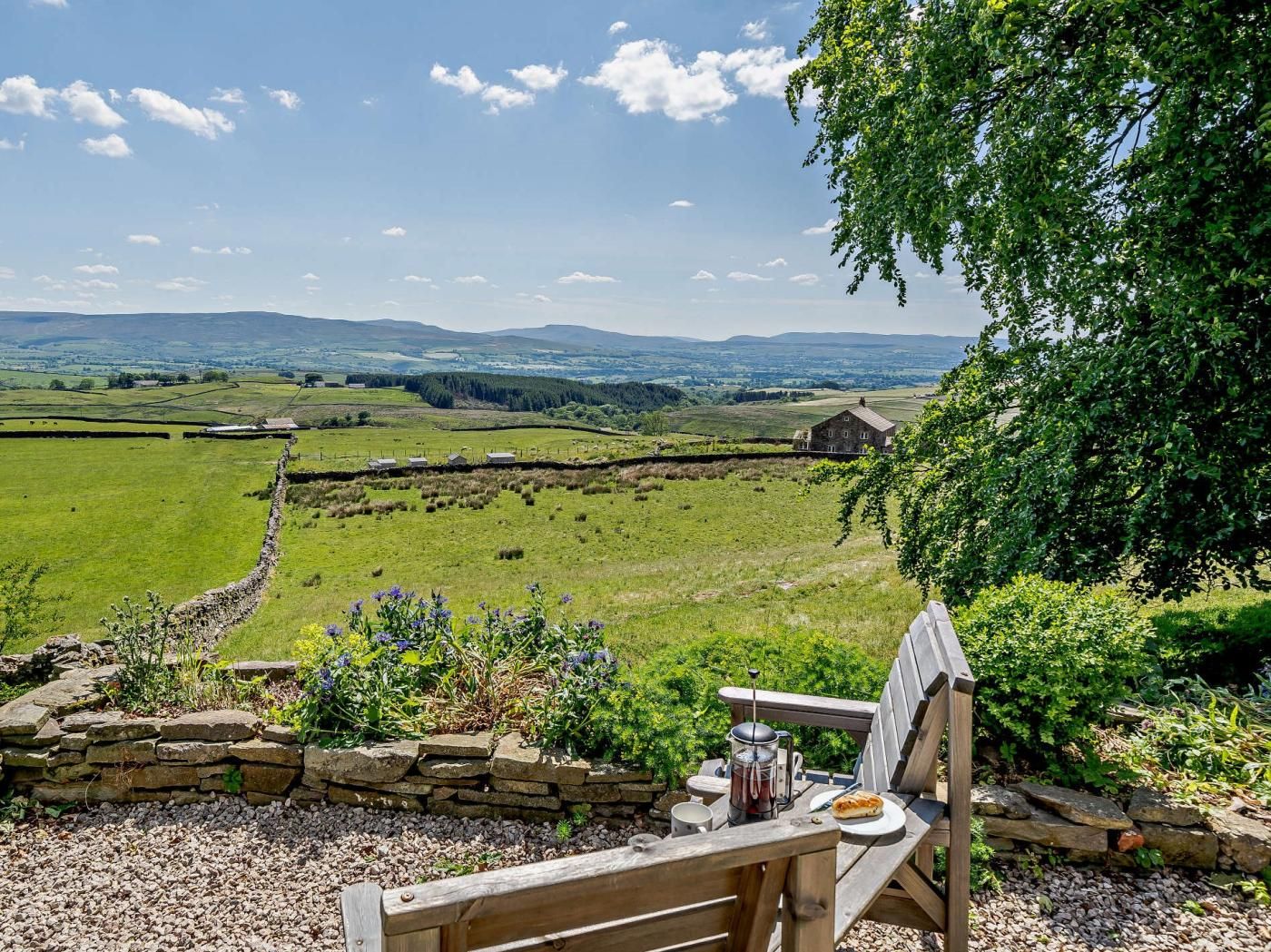 A wooden bench with a stone wall and a view of a rural landscape.