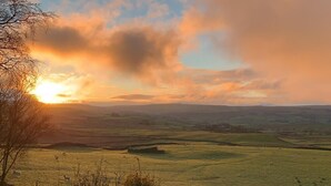 Un paysage rural avec des collines ondoyantes et un coucher de soleil.