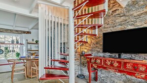 A modern interior with a spiral staircase, a stone wall, a TV, and a dining area with a view. - 3 Bed in Fowey (oc-92548) (Fowey)