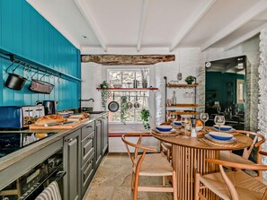 Une cuisine avec des placards bleus, une table à manger en bois avec des chaises et une grande fenêtre.