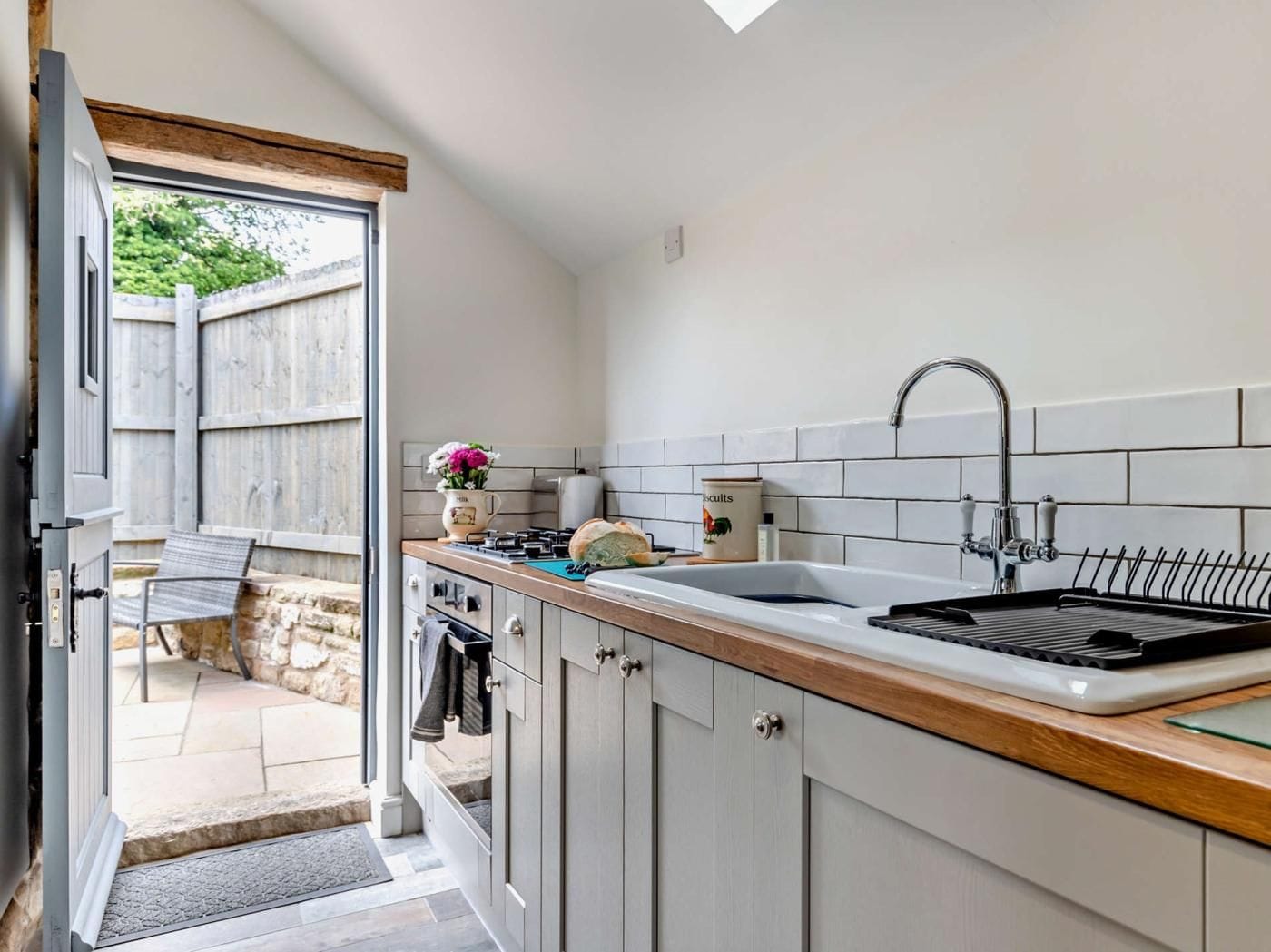 Eine moderne Küche mit eingebautem Backofen, einem Spülbecken mit Armatur und einem Fenster mit Blick auf einen Garten.