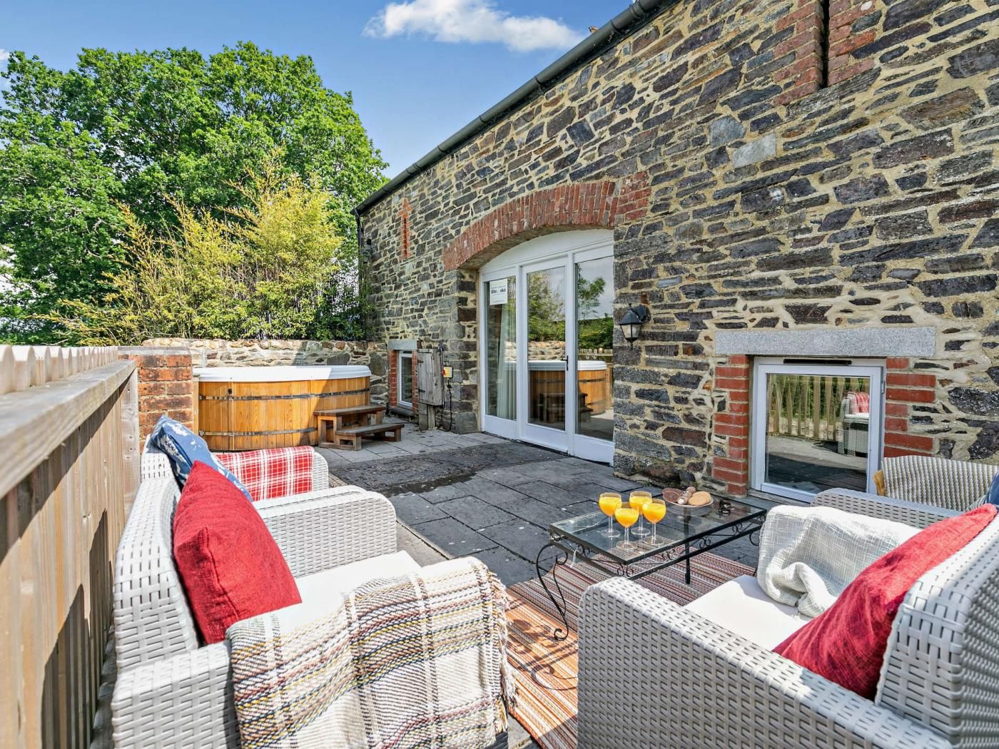 An outdoor patio with wicker furniture, a hot tub, and a stone building with a glass door.