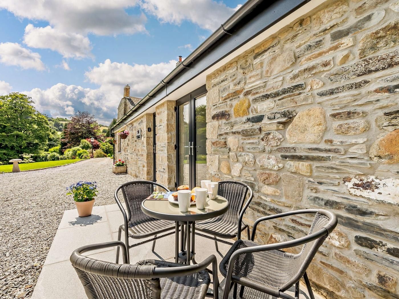 Un bâtiment en pierre doté d’un patio aménagé avec des meubles en osier, une table, des tasses et une assiette.