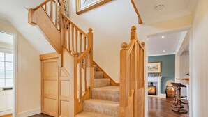 Un escalier en bois, dont les marches sont recouvertes de moquette, mène à un palier. On y trouve une porte en bois et une cheminée avec une manteau de cheminée.