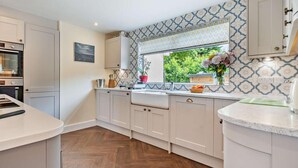Une cuisine moderne avec des meubles blancs, un parquet en bois disposé en chevrons et une fenêtre donnant sur un espace verdoyant.