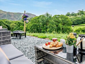 An outdoor seating area with a table set for a meal, a wicker chair, and a view of a green landscape. - 1 Bed in Penrith (oc-92641) (Deepdale)