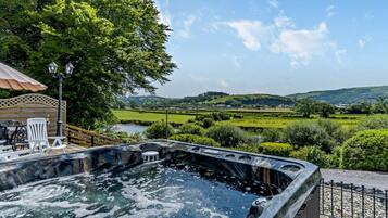 A hot tub with a view of a river and hills, outdoor seating, and a pergola.