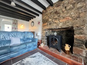 A living room with a stone fireplace, a blue leather sofa, and a tiled floor. - 2 Bed in Pwllheli (oc-92561) (Llithfaen)