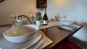 A dining table set with white plates, bowls, and wine glasses, a bottle of wine, and a small potted plant. - 2 Bed in Pwllheli (oc-92561) (Llithfaen)