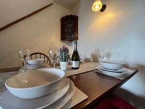 Ein Esstisch mit weißen Tellern, Schüsseln und Weingläsern, einer Weinflasche und einem kleinen Blumentopf.