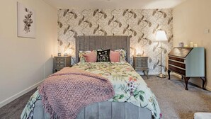 Een slaapkamer met een bed, nachtkastjes, een lamp, een dressoir en een wand met een bloemenprint.
