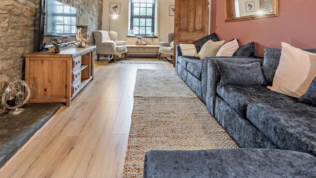 Een woonkamer met een stenen muur, houten meubels, een ruime bank, een houten kast en een televisie.