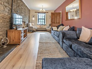 Una sala de estar con pared de piedra, muebles de madera, un sofá grande, un aparador de madera y un televisor.