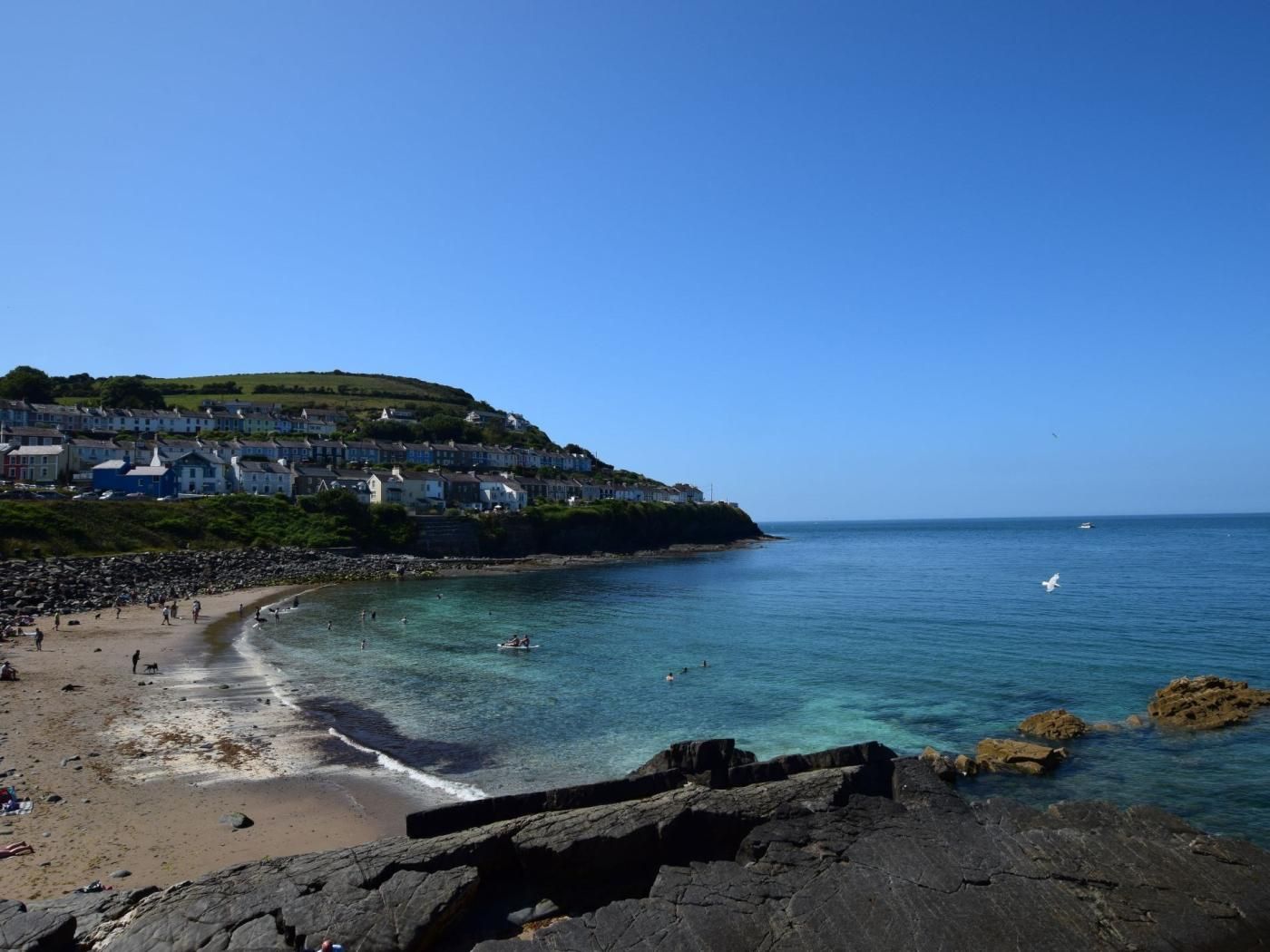 Un pueblo costero con playa, costa rocosa y casas en una colina.