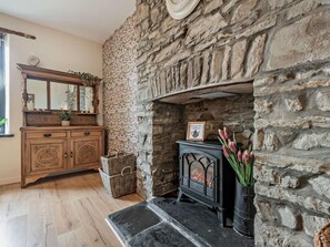 A stone fireplace with a black stove, a wooden dresser with a mirror, and a wicker basket. - 3 Bed in Llandysul (oc-92525) (Llandysul)
