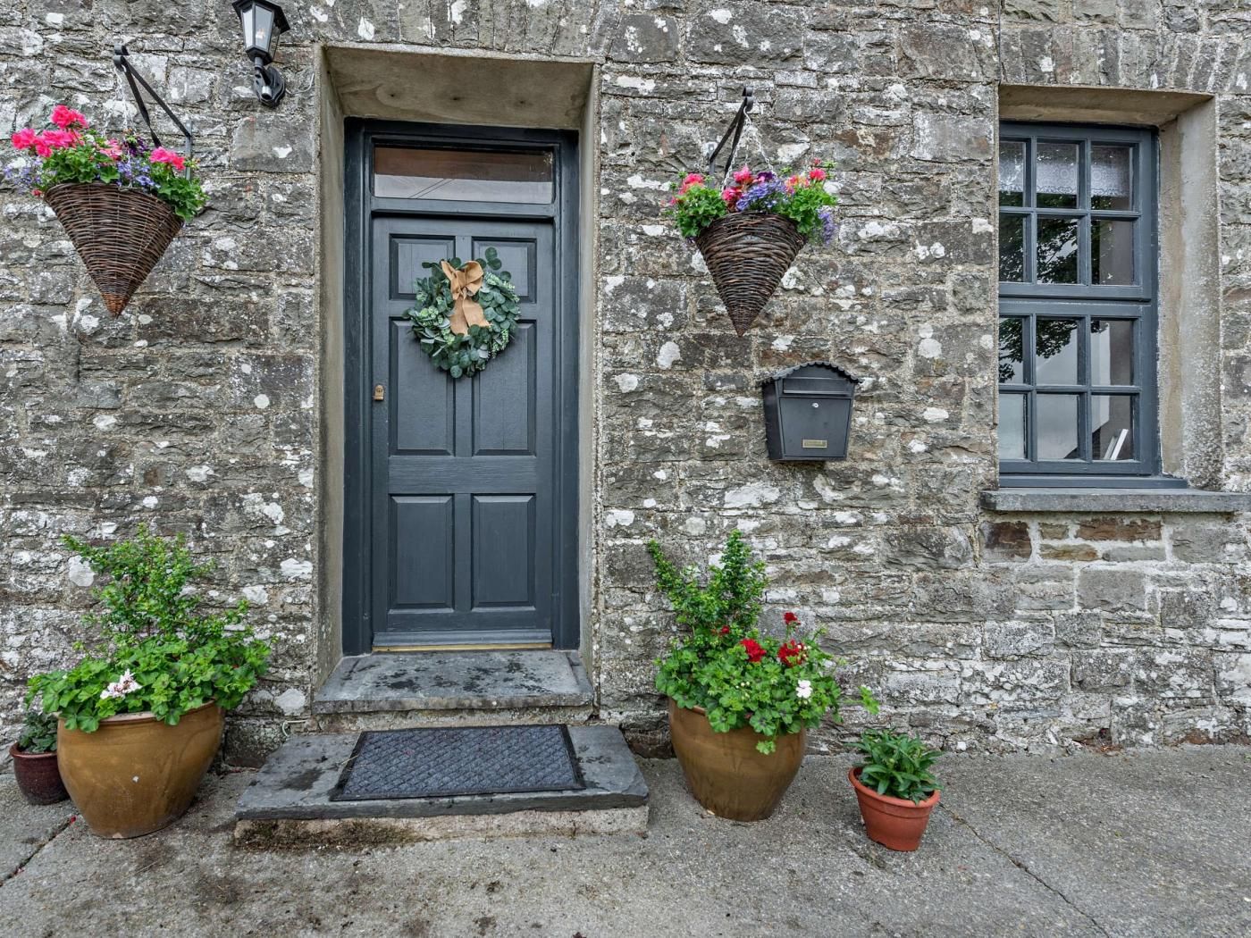 A stone building with a dark door, two flower baskets, and a mailbox.