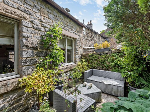 Un bâtiment en pierre doté d’un patio-jardin aménagé avec des meubles en osier et des plantes en pot.