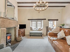 Ein gemütliches Wohnzimmer mit Kamin, Fernseher, einer bequemen Couch und einem Kronleuchter.