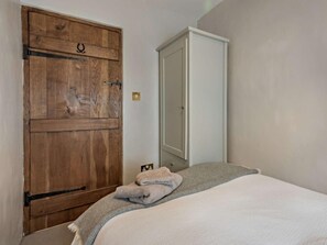 Une chambre avec une armoire en bois, une armoire blanche et un lit recouvert d’une couverture grise.
