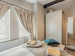 Ein Schlafzimmer mit Bett, Schrank, Heizkörper und einem Fenster mit Vorhängen.