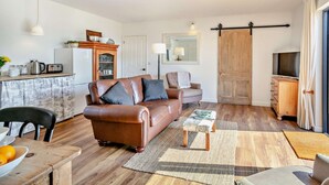 A living room with a brown leather sofa, a wooden coffee table, and a kitchen area with a refrigerator, toaster, and cabinets. - 2 Bed in Barnstaple (oc-92653) (Barnstaple)
