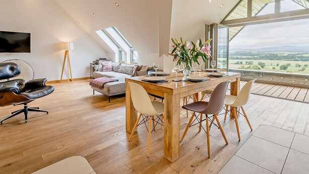 Ein geräumiges Loft mit Essbereich, einer Couch, einem Fernseher und Blick ins Grüne.