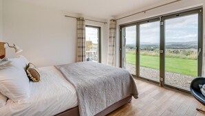 Ein Schlafzimmer mit einem großen Bett, einem Schreibtisch und Blick auf eine grüne Landschaft durch eine Schiebetür.