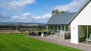 Ein modernes Haus mit Terrasse, Sitzgelegenheit im Freien und Blick ins Grüne.