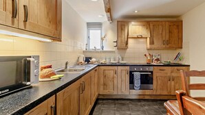 Une cuisine avec des meubles de rangement en bois, une cuisinière, un évier et un four à micro-ondes.