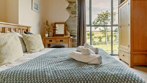 Une chambre à coucher avec une couvre-lit à motifs, un bureau en bois doté d’un miroir et une vue sur l’extérieur grâce à une grande fenêtre.