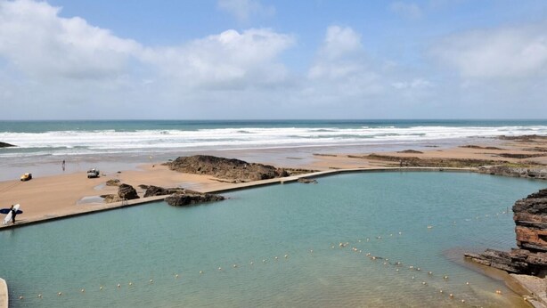 Un paysage côtier avec un ciel dégagé, une plage et une piscine artificielle.