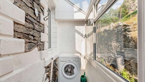Une petite buanderie comprenant un lave-linge, une fenêtre et un mur en pierre.