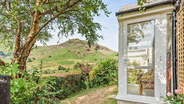 Une véranda offrant une vue sur une colline, un sentier de jardin et un fauteuil en osier.