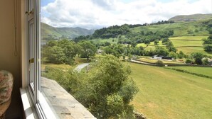 Une pièce dotée d’une grande fenêtre donnant sur une vallée verdoyante, avec des maisons et une rivière.