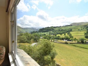 Ein Zimmer mit einem großen Fenster mit Blick auf ein grünes Tal mit Häusern und einem Fluss.