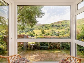 Ein Zimmer mit großem Fenster und Blick auf ein grünes Tal und Hügel.