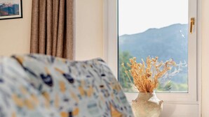 Une pièce avec un canapé, un vase contenant des plantes séchées et une fenêtre donnant sur la montagne.