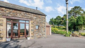 A stone building with a large glass door, a small attached shed, and a gravel driveway. - 3 Bed in Wigton (oc-92500) (Uldale)