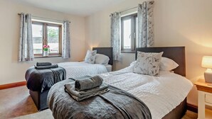 A double room with two beds, a window with curtains, a bedside table with a lamp, and a towel on the bed. - 3 Bed in Wigton (oc-92500) (Uldale)