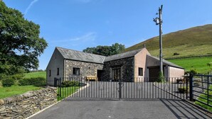 A stone building with a metal gate, a stone wall, and a grassy field in the background. - 3 Bed in Wigton (oc-92500) (Uldale)