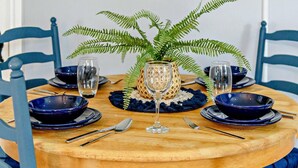 Uma mesa de jantar redonda de madeira com cadeiras azuis, uma planta samambaia no centro e um vaso de vidro decorativo.