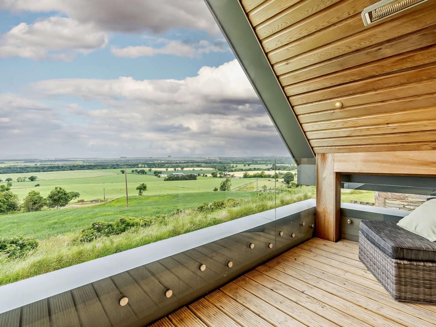 Ein Balkon mit Blick auf eine grüne Landschaft und einen bewölkten Himmel.