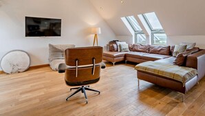Ein geräumiger Loft mit hohen Decken, einem großen Fenster, einem Ledersofa, einem Holzstuhl und einem Flachbildfernseher.