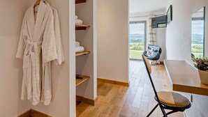 Ein modernes Badezimmer mit einem Holzwaschtisch, einem an der Wand hängenden Bademantel und Ausblick ins Freie durch ein großes Fenster.