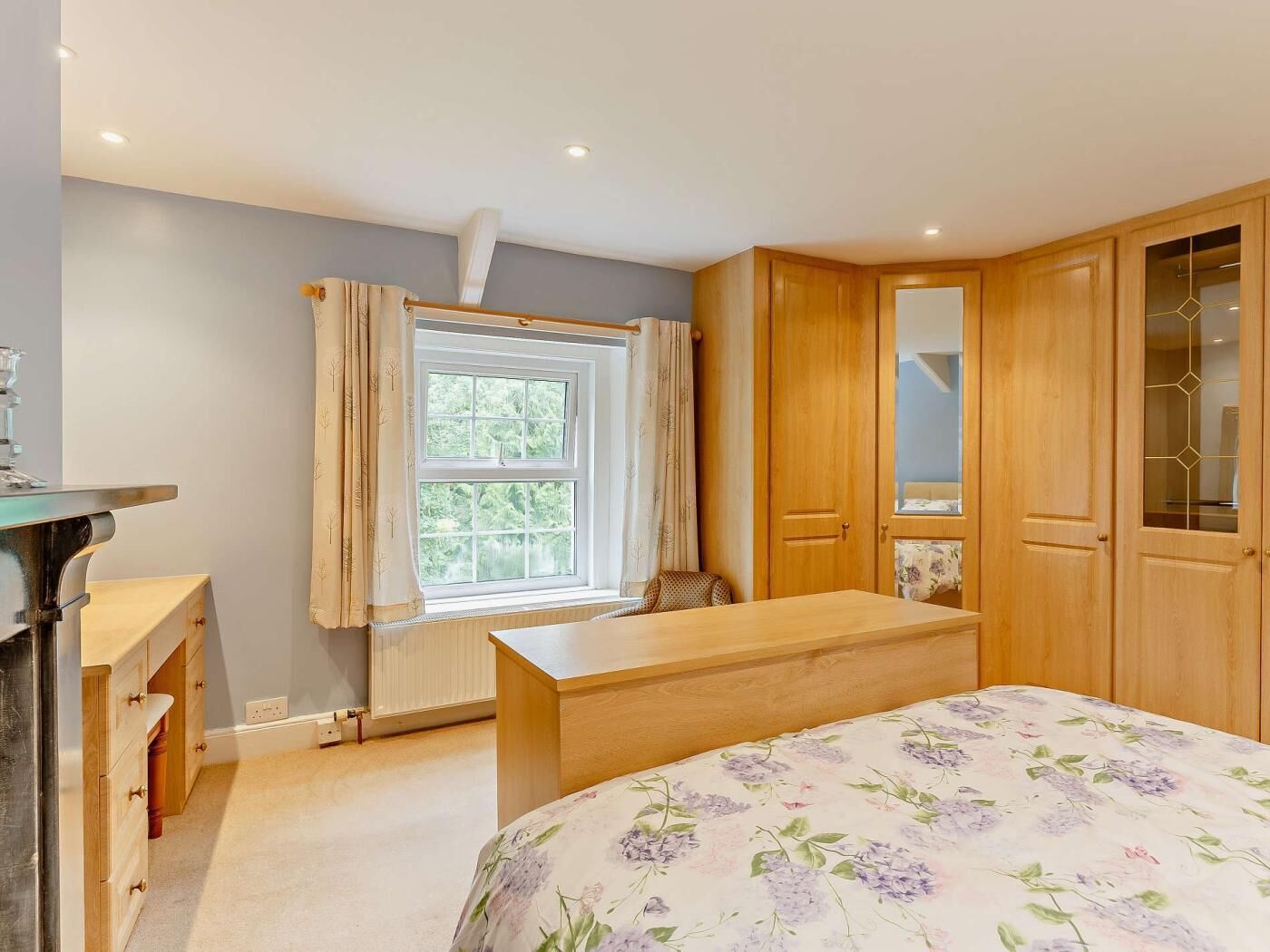 A bedroom with a bed, a desk, a chair, a radiator, a window with curtains, and wooden doors.