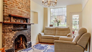 A living room with a brick fireplace, a sofa, a chair, and a chandelier. - 4 Bed in Tavistock (oc-92491) (Gulworthy)